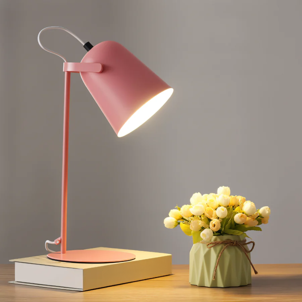Pink desk lamp on a wooden surface with a small potted plant.