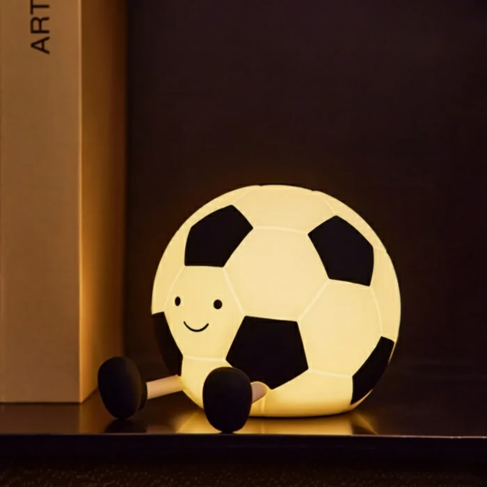 Soccer ball-shaped night light with a smiling face on a dark surface.