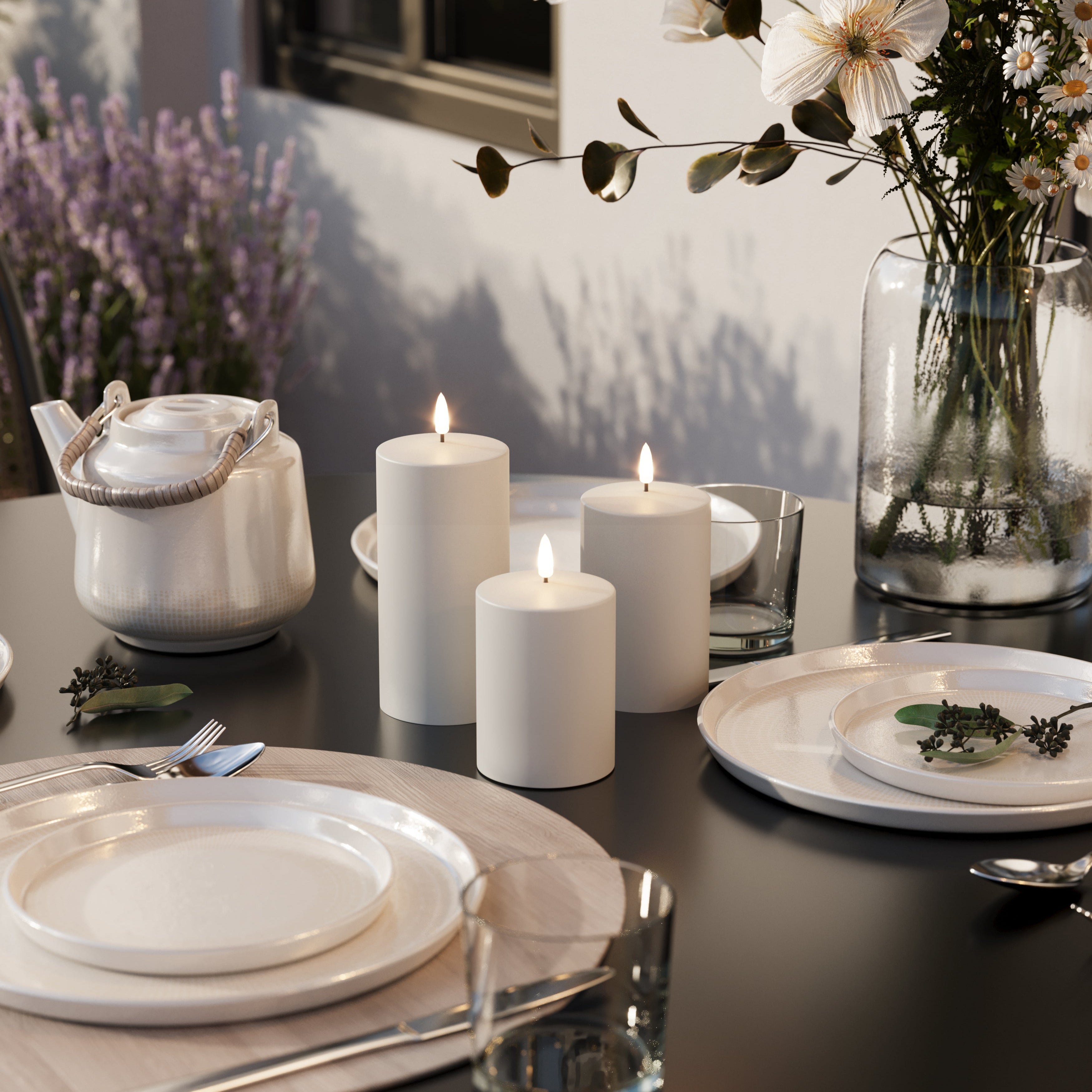 Elegant table setting with candles, flowers, and teapot on a dark surface.
