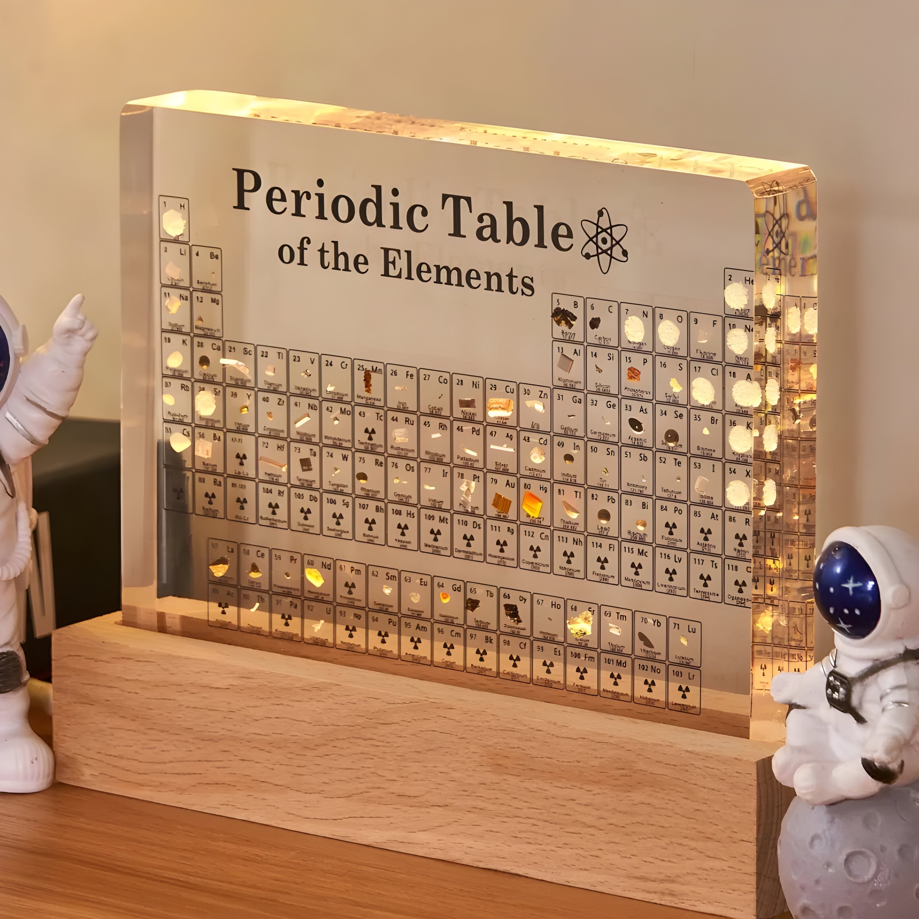 Lighted periodic table of elements display with wooden base and small figurines on a wooden surface.