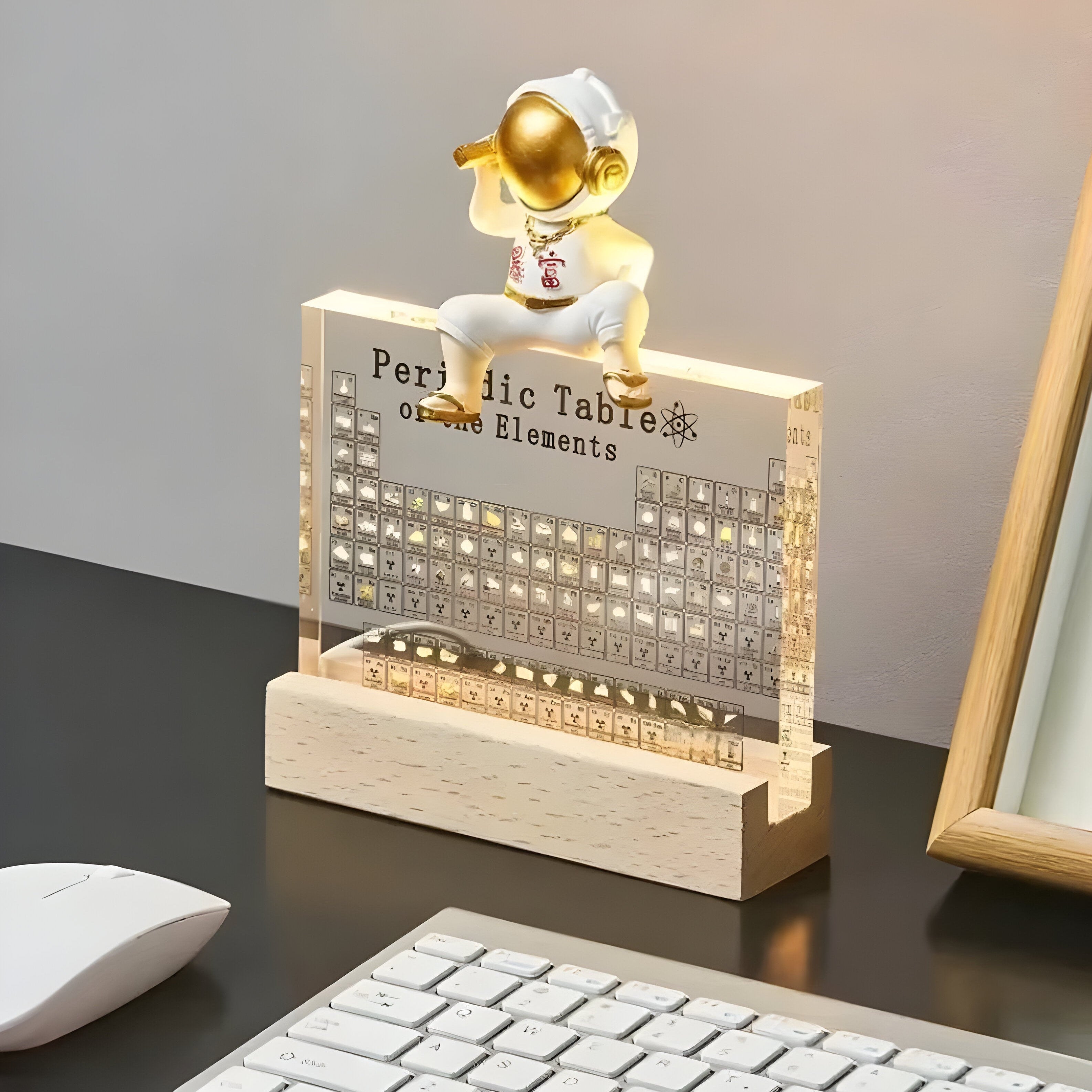 Decorative desk lamp with periodic table design and small figure on a wooden base.