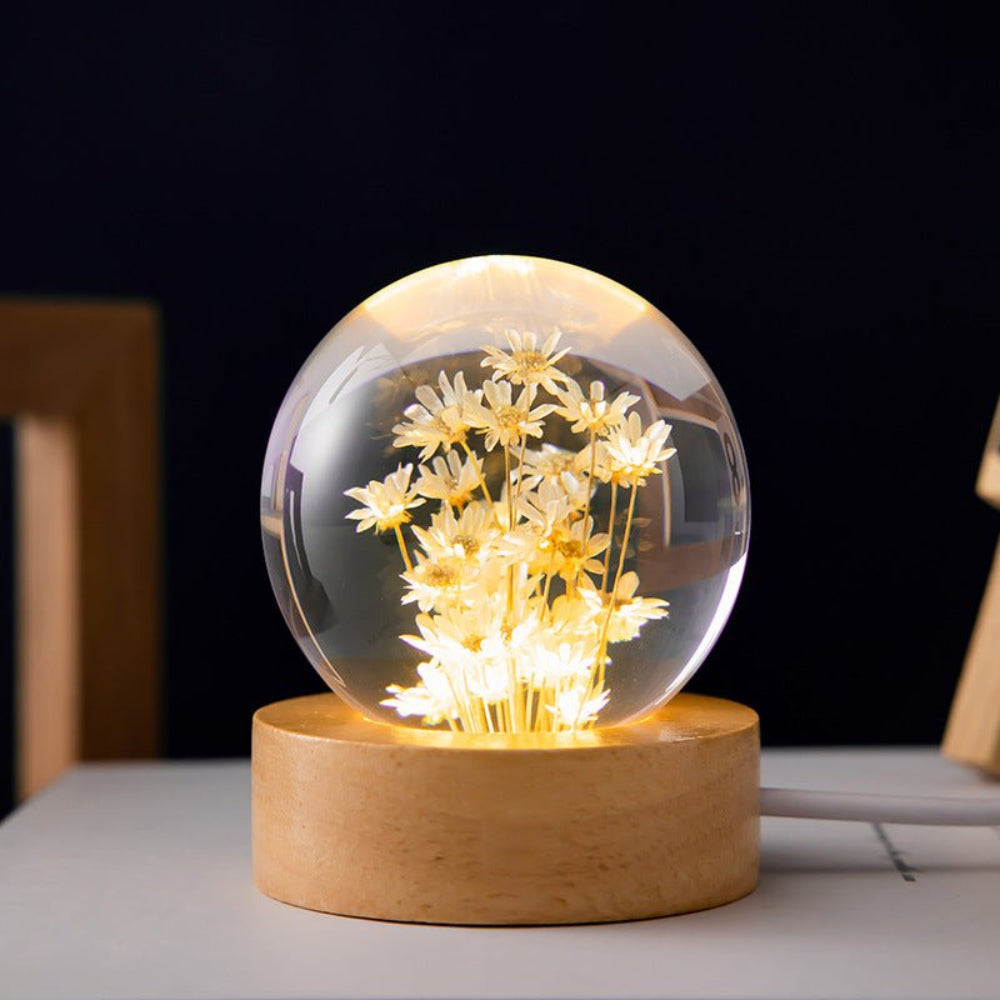 Glass sphere with illuminated flowers on a wooden base against a dark background