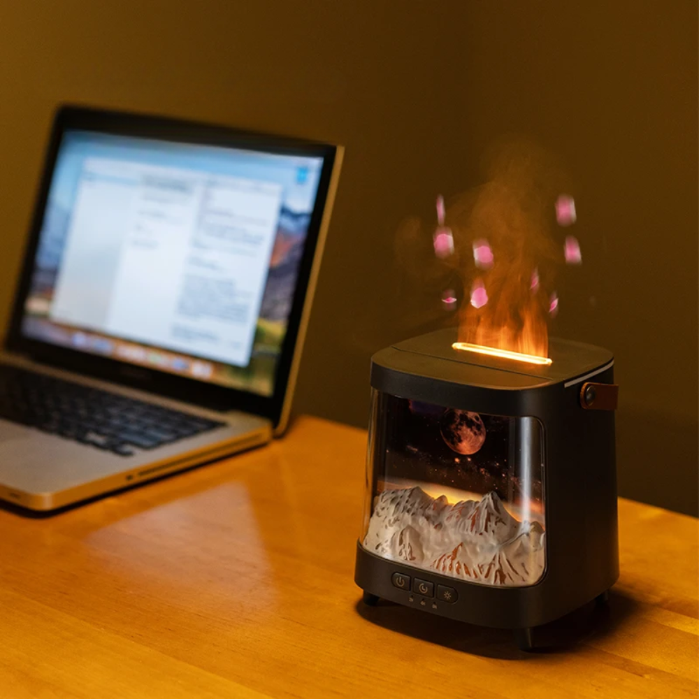 Laptop on a desk with a small decorative lamp showing a mountain and flame design.