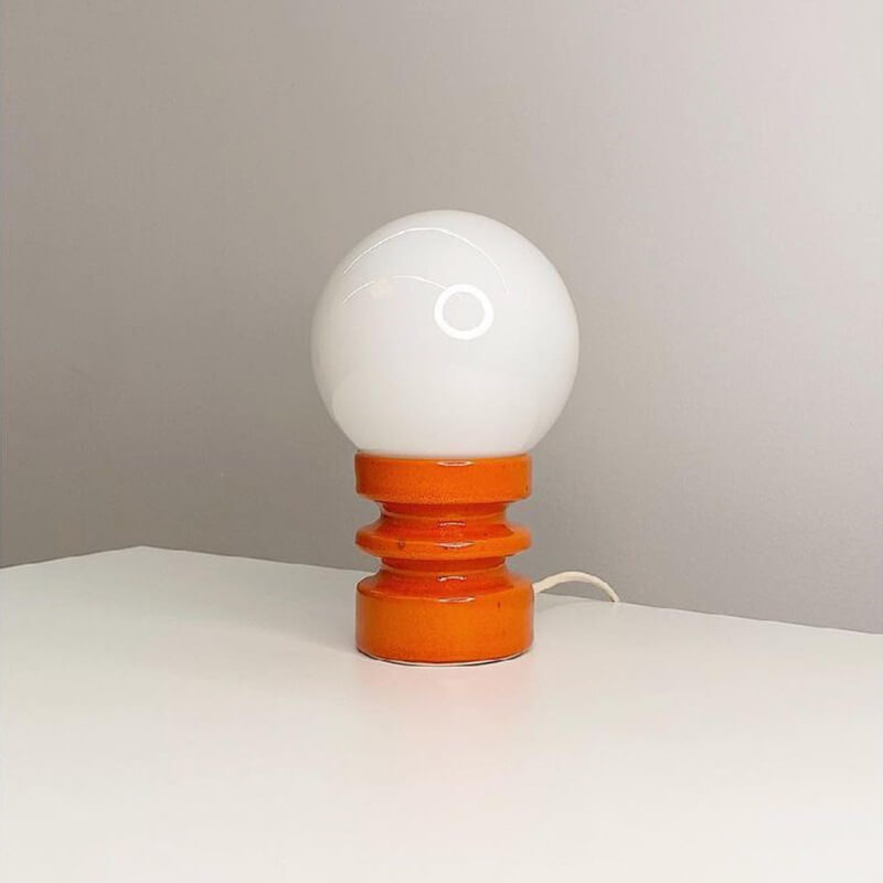 Table lamp with a white bulb and orange base on a neutral background