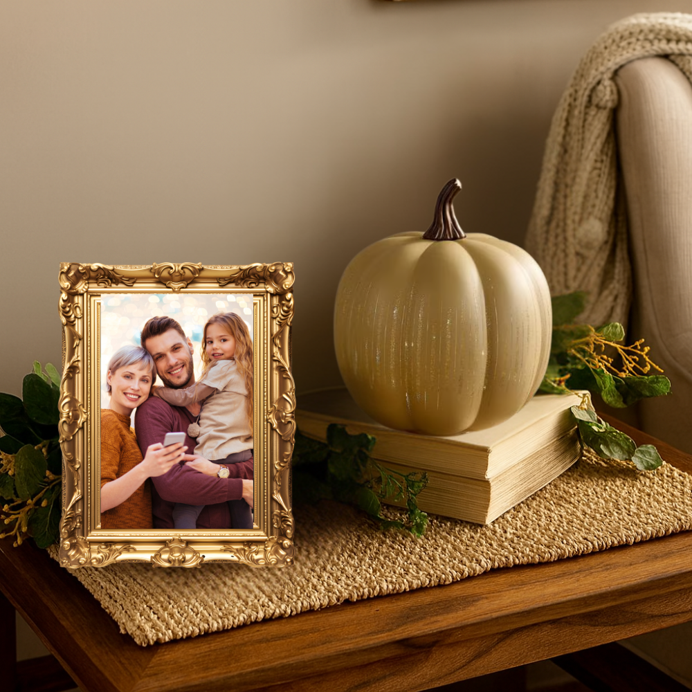 Decorative setup with a gold-framed photo of a family, a beige pumpkin on books, and greenery on a wooden surface.