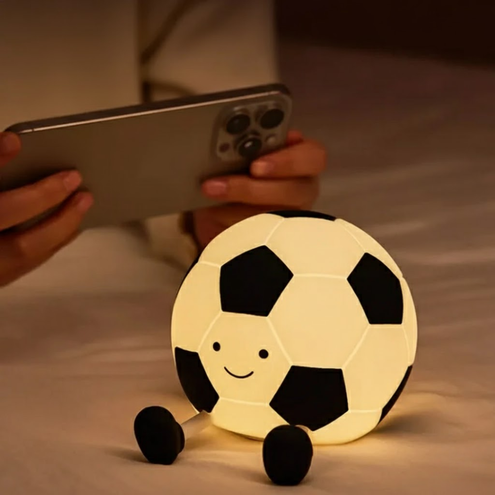 Glowing soccer ball with wheels on a soft surface, person using phone in background