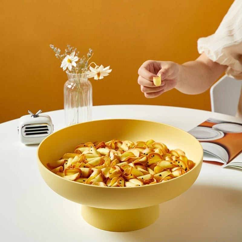 Yellow bowl filled with pasta on a table with a vase and small radio in the background.