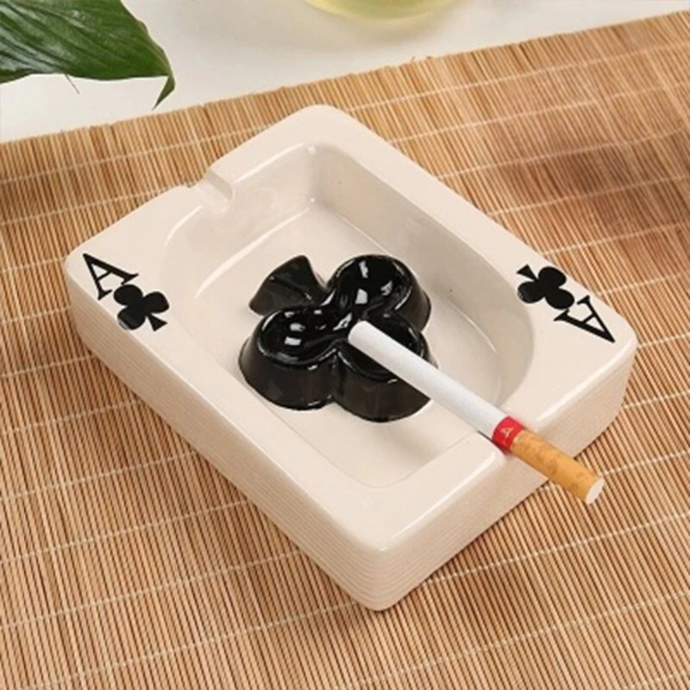 White ceramic ashtray with black floral design on a woven mat, featuring a cigarette.