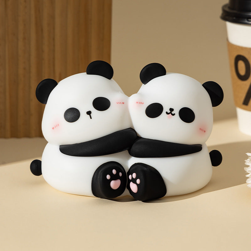 Two panda-shaped squishies hugging on a beige surface with a blurred coffee cup in the background.