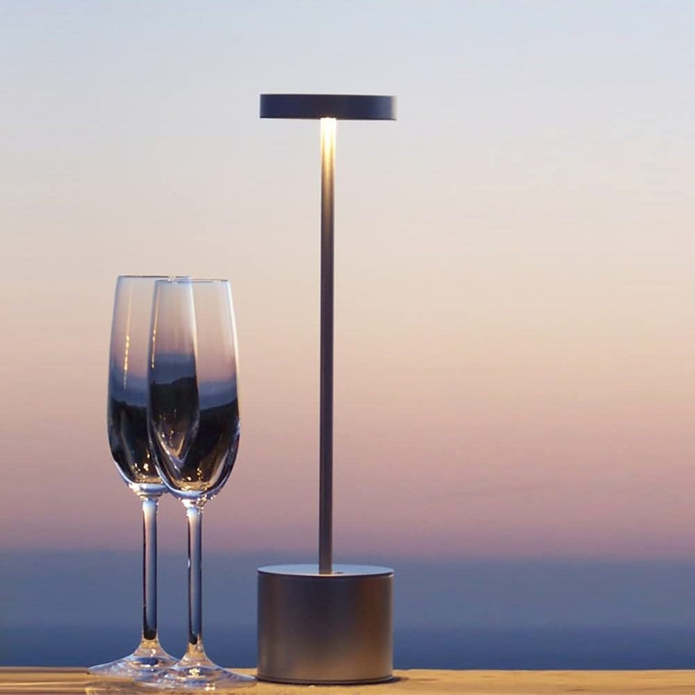 Solar lamp with two wine glasses on a wooden surface against a sunset sky.