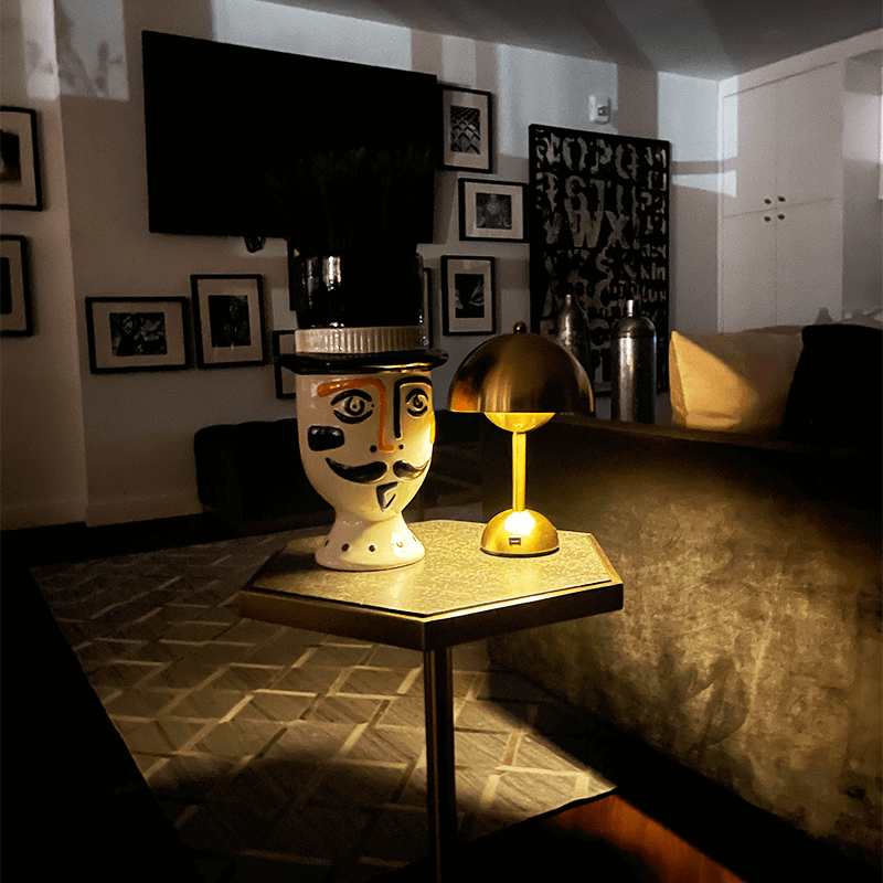 Decorative lamp with face design on a table in a room with framed pictures on the wall.