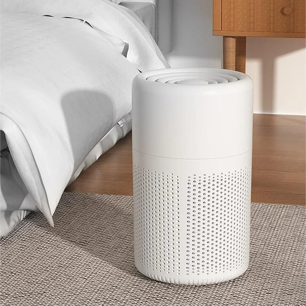 White cylindrical air purifier on a carpeted floor next to a bed