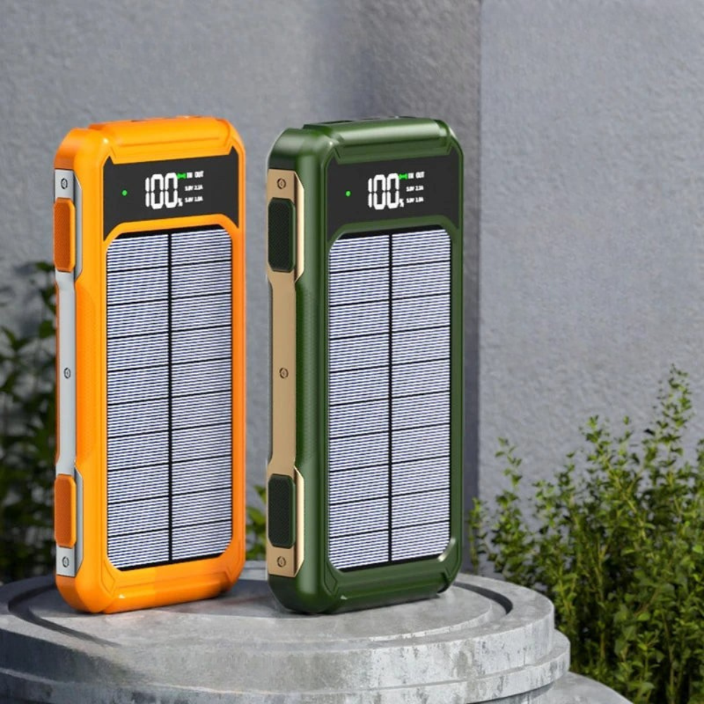 Two solar-powered portable chargers, one orange and one green, on a stone surface with a gray wall and plants in the background.