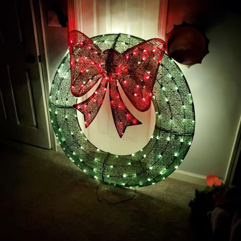 Decorative wreath with red bow and green lights in a dimly lit room.