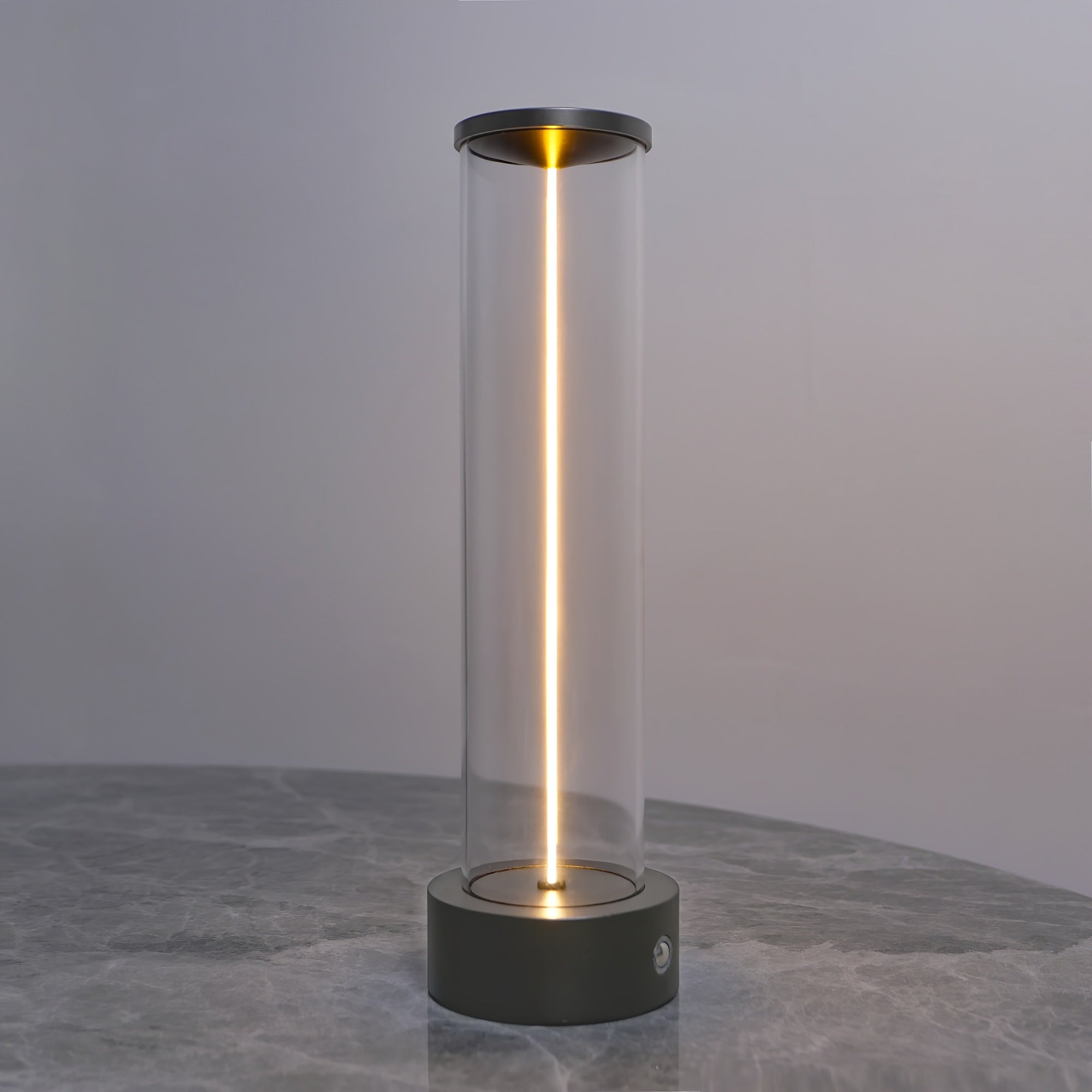 Cylindrical lamp with clear glass and black base on a gray surface