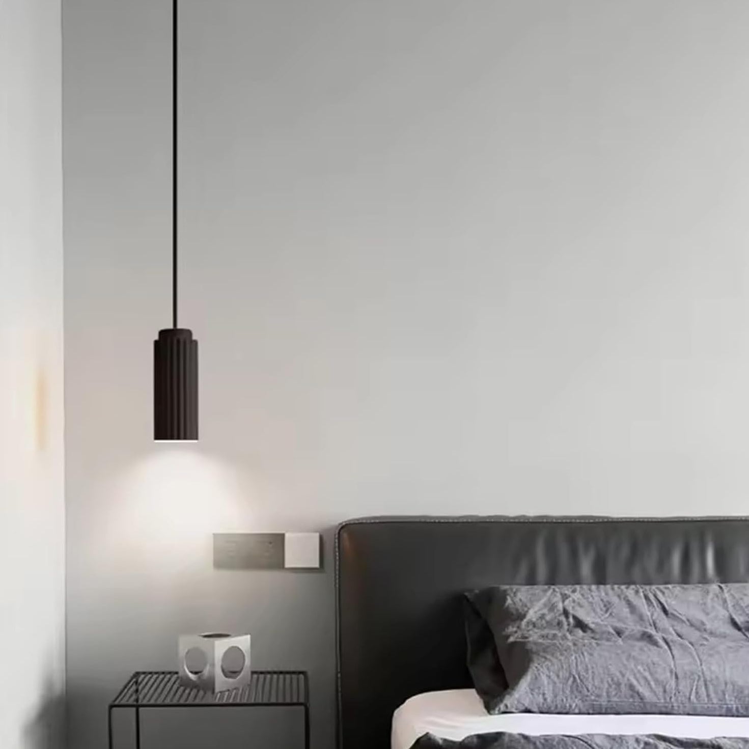 Modern pendant light hanging above a bed in a bedroom setting.