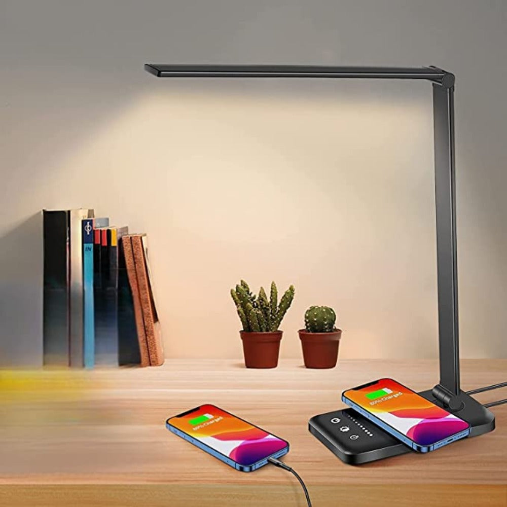 Desk lamp with wireless charging pad on a wooden surface with books and plants.