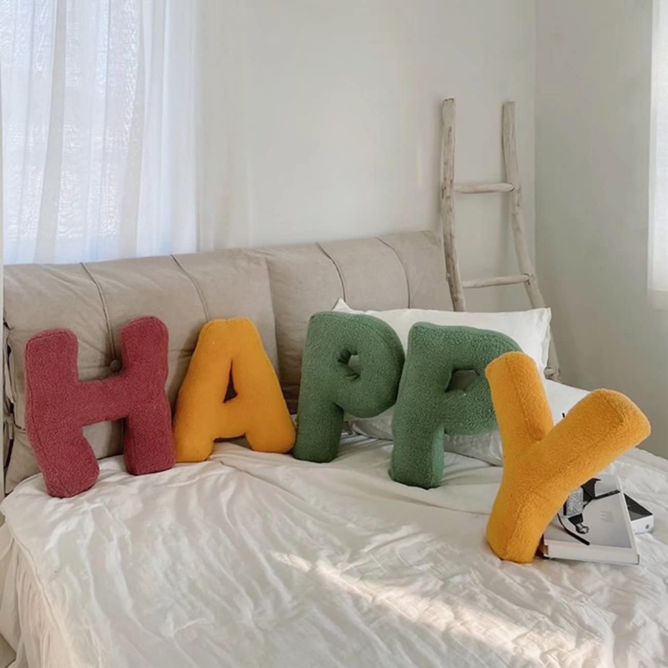 Colorful letter-shaped cushions spelling 'HAPPY' on a bed with a ladder in the background.