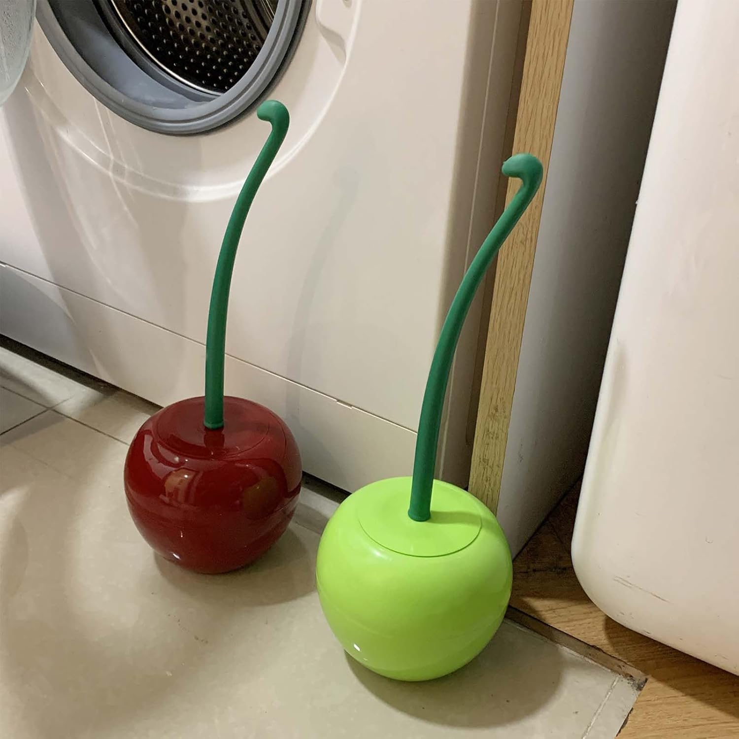 Two colorful cherry-shaped cleaning tools on a floor next to a washing machine.