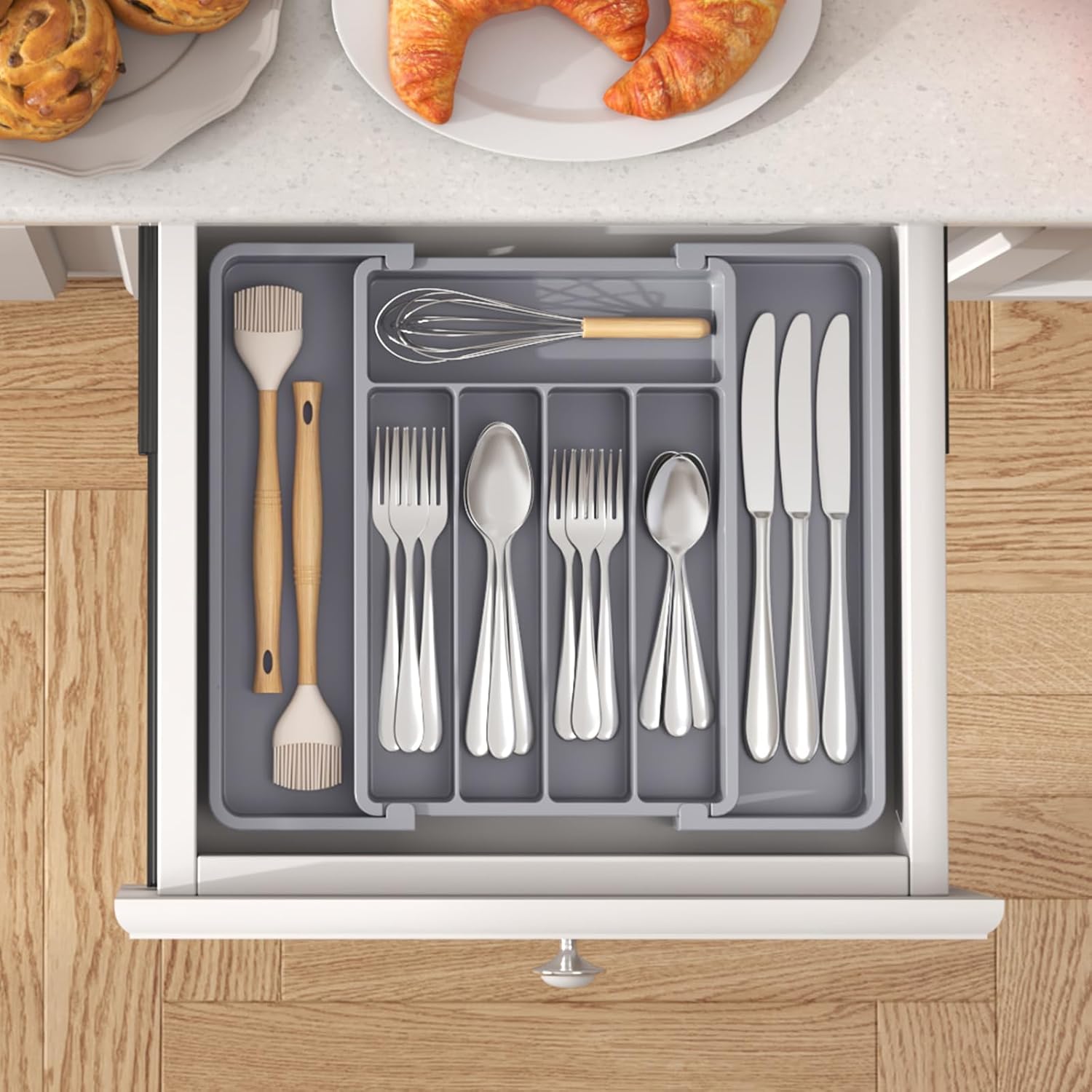 Open kitchen drawer with cutlery organizer and utensils on a wooden floor.