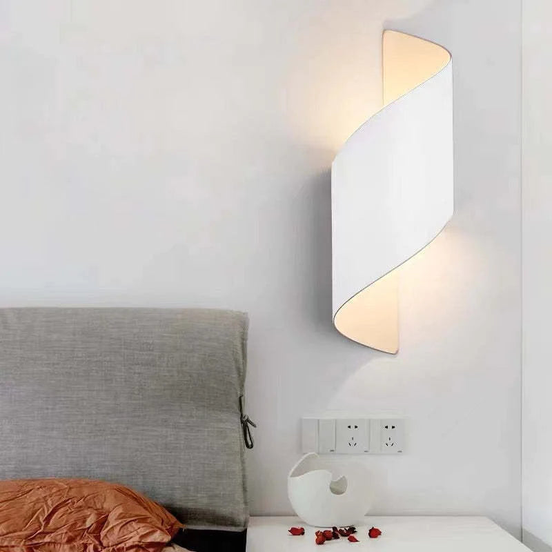 Modern wall lamp on a white wall above a bed with a gray headboard.