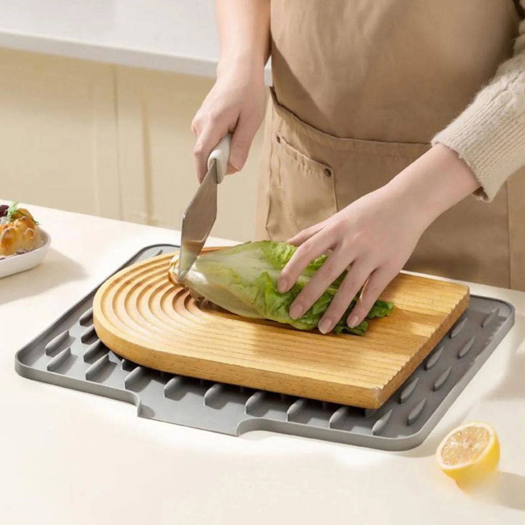 Person cutting lettuce on a wooden cutting board with a gray silicone mat underneath