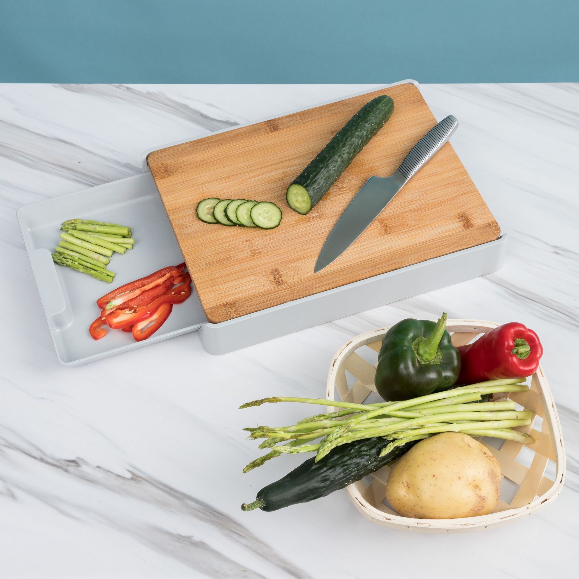 Wooden cutting board with sliced cucumber, knife, and vegetables on a marble surface