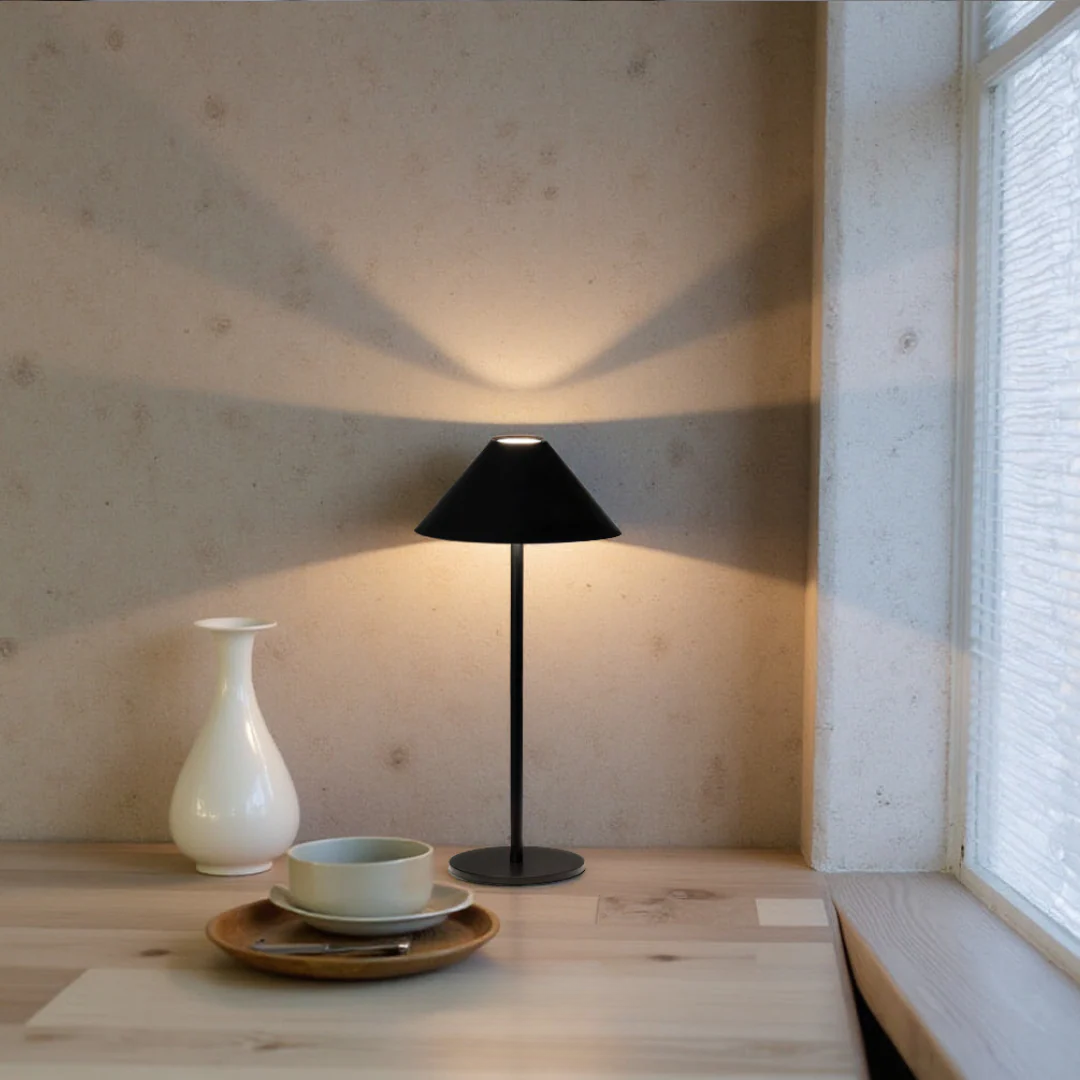 Black table lamp on a wooden surface with a white vase and bowl.