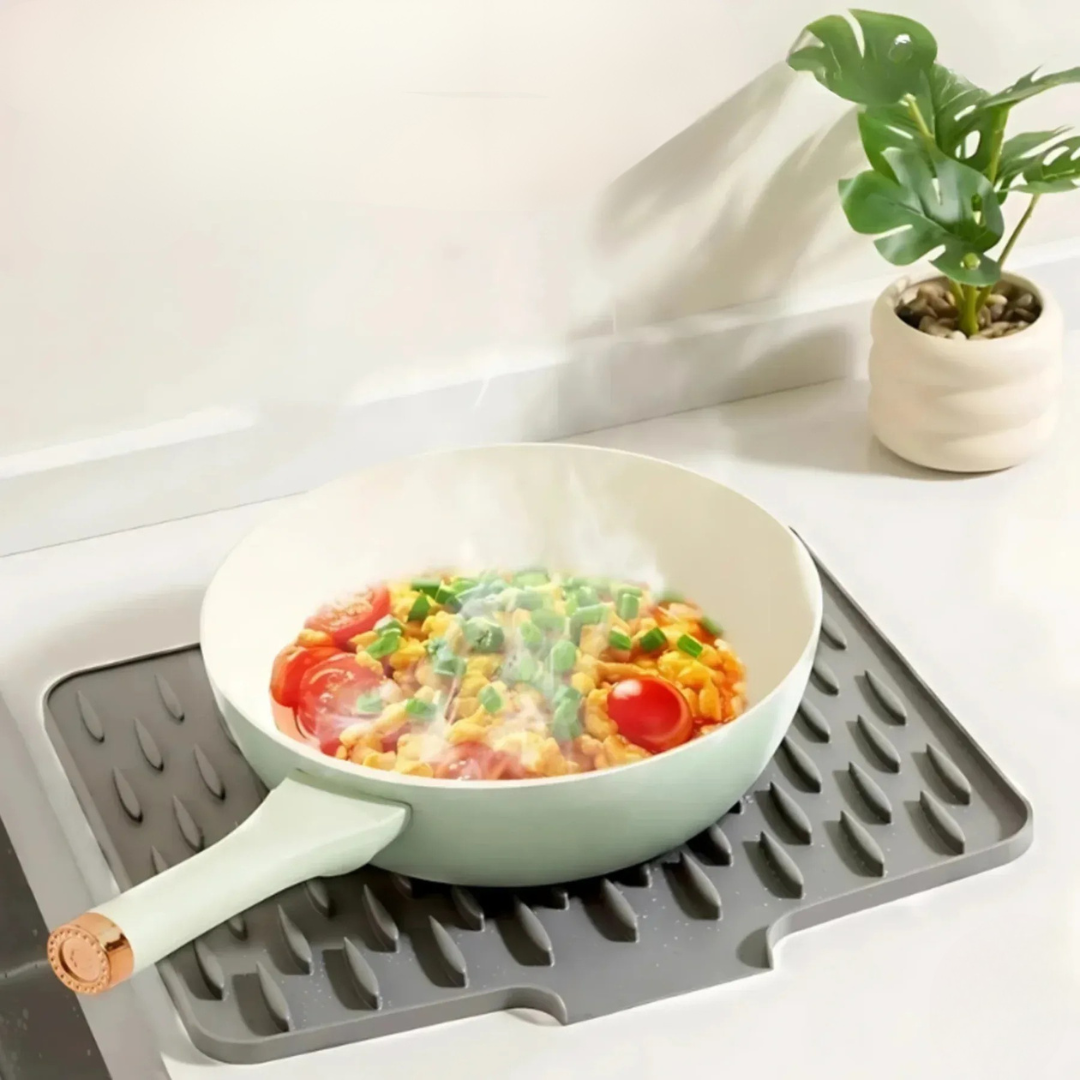 Frying pan with colorful vegetables on a gray silicone mat on a kitchen counter.
