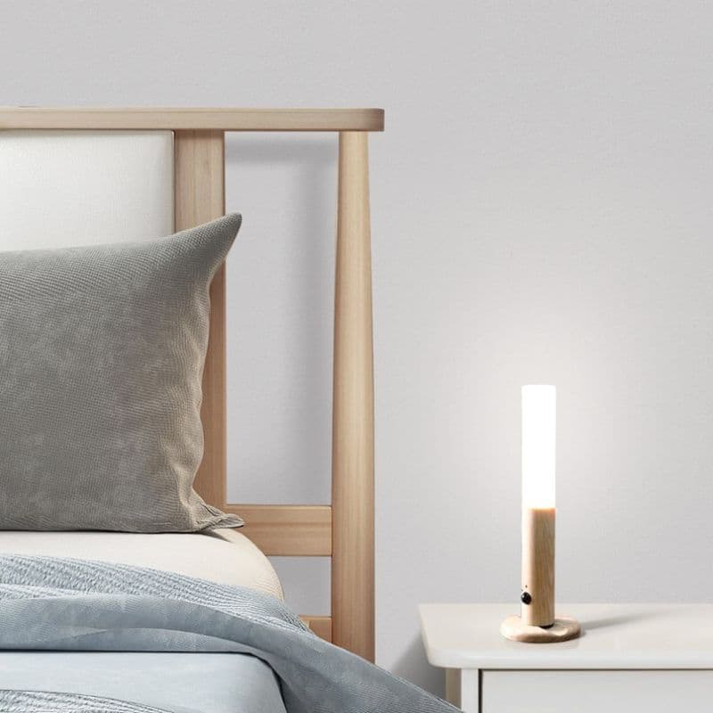 Bed with wooden headboard and gray pillow, nightstand with lamp against light gray wall