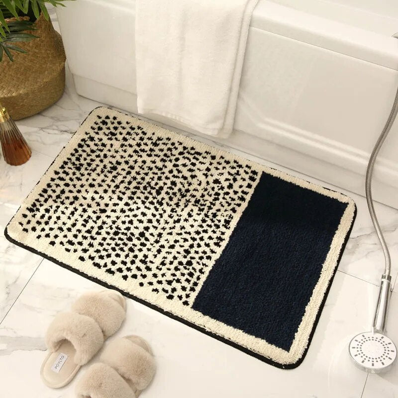 Bath mat with black and white pattern on a bathroom floor with slippers and shower head.