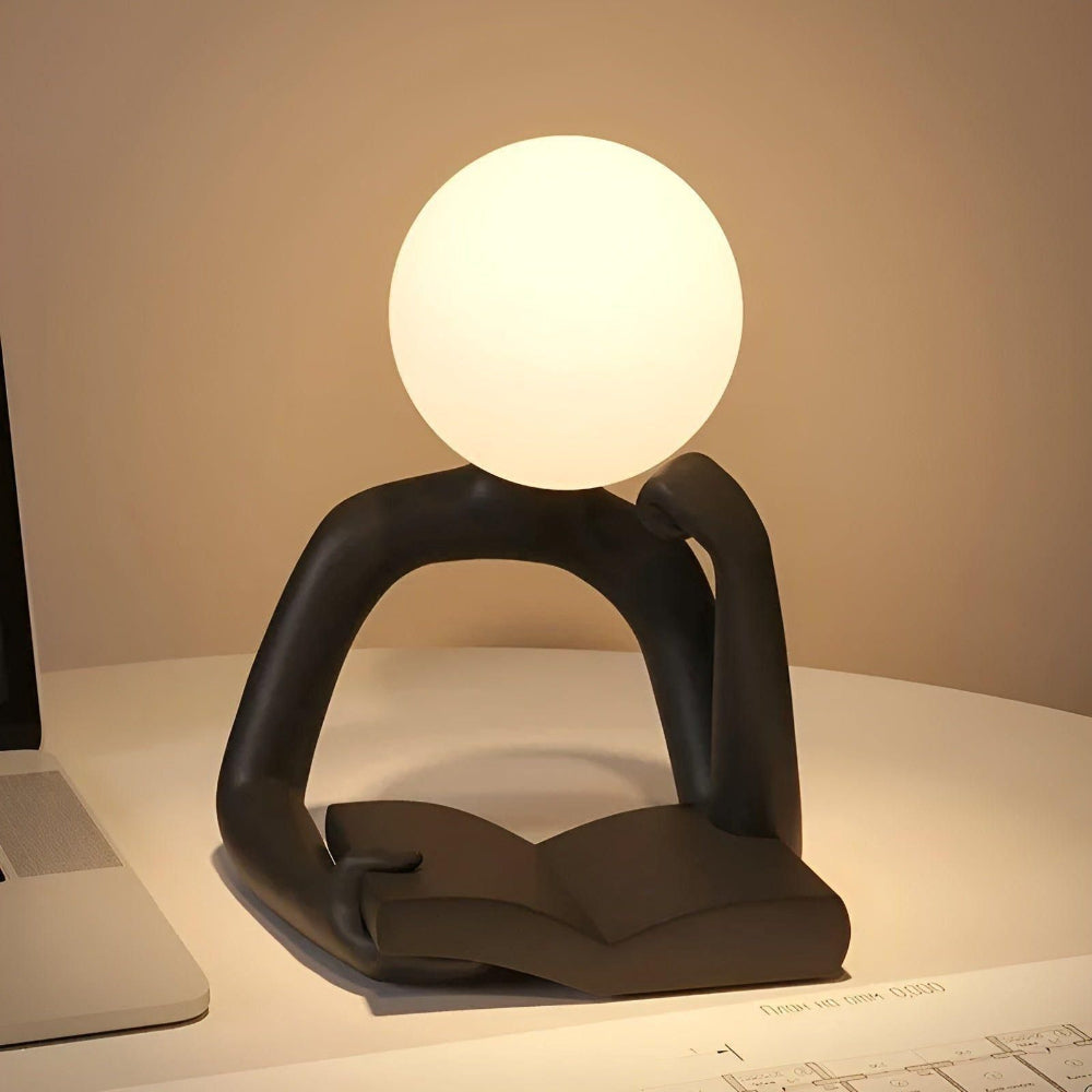 Modern table lamp with a spherical light bulb on a desk next to a laptop.