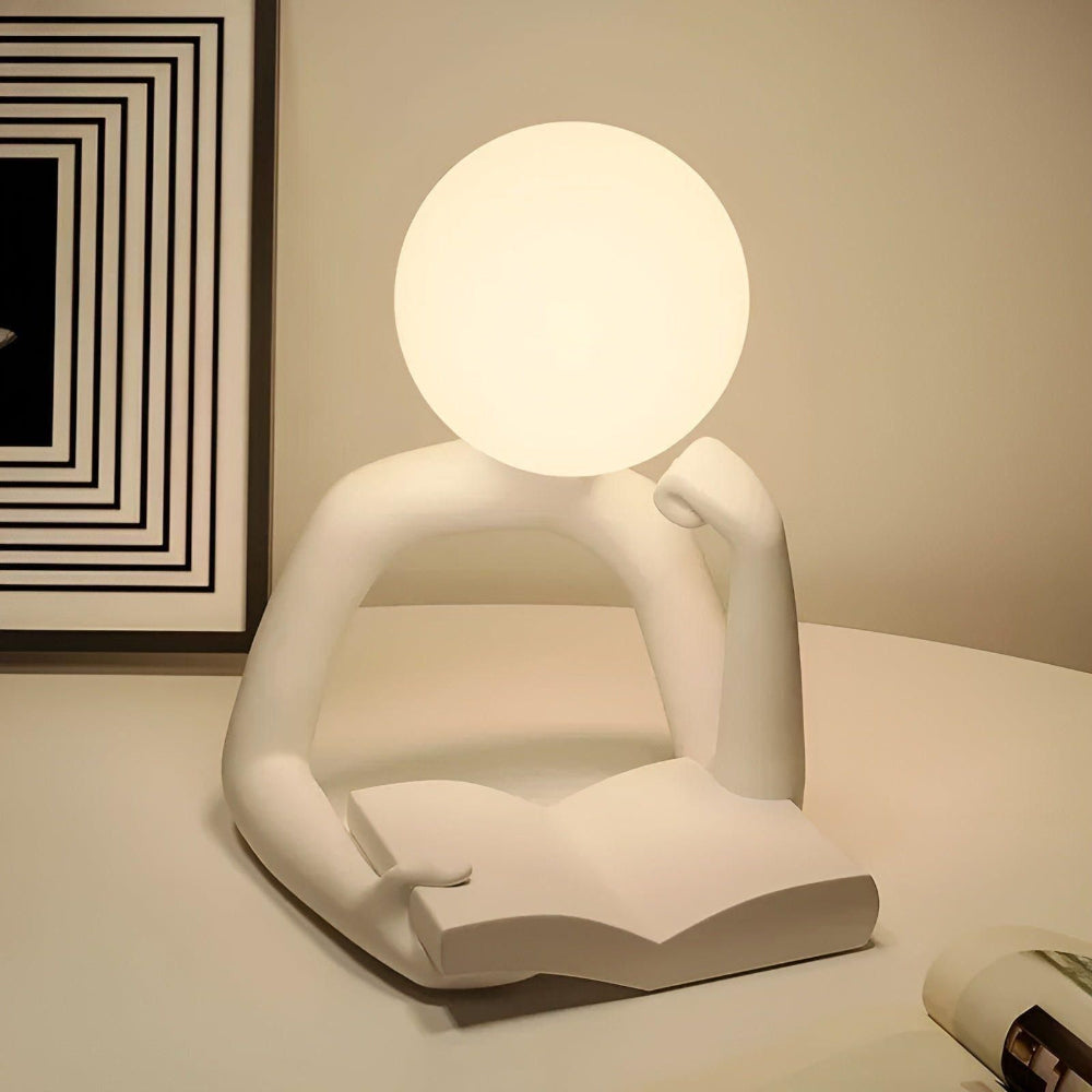 Modern lamp shaped like a person reading a book with a round light bulb for a head, on a neutral background.