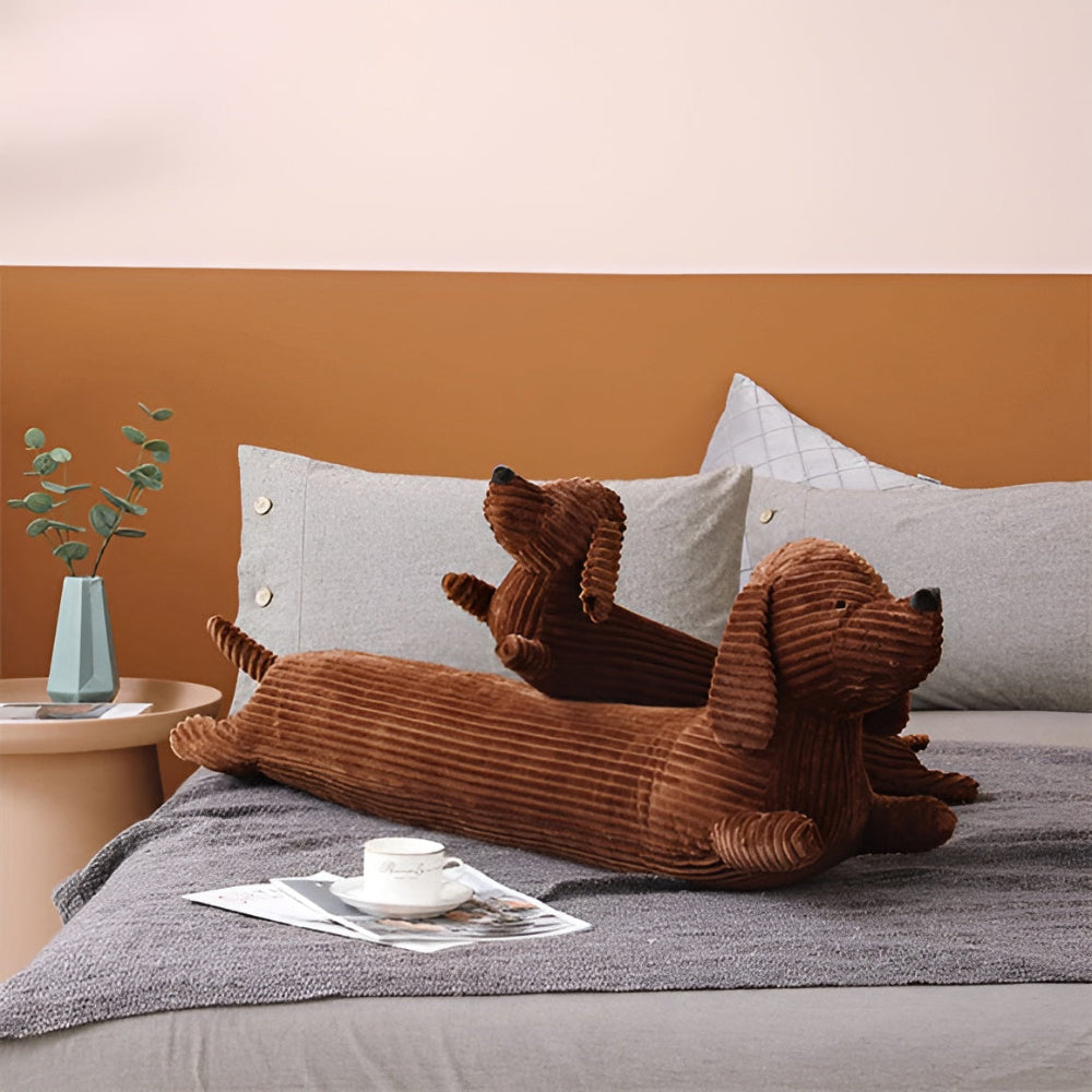 Brown dog-shaped cushion on a bed with a coffee cup and newspaper