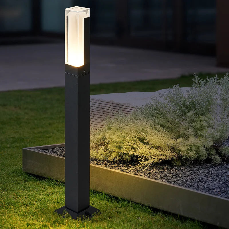 Black outdoor lamp post illuminating a garden area at night.