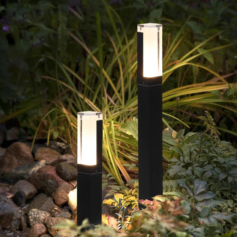 Two black garden lights with white cylindrical lamps on a garden background.