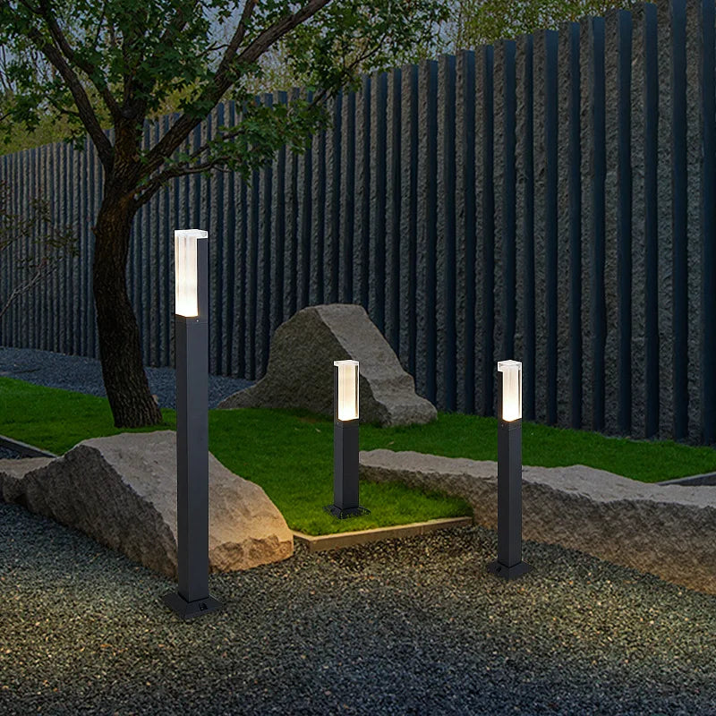 Garden setting with three illuminated outdoor lamps on grass and rocks.