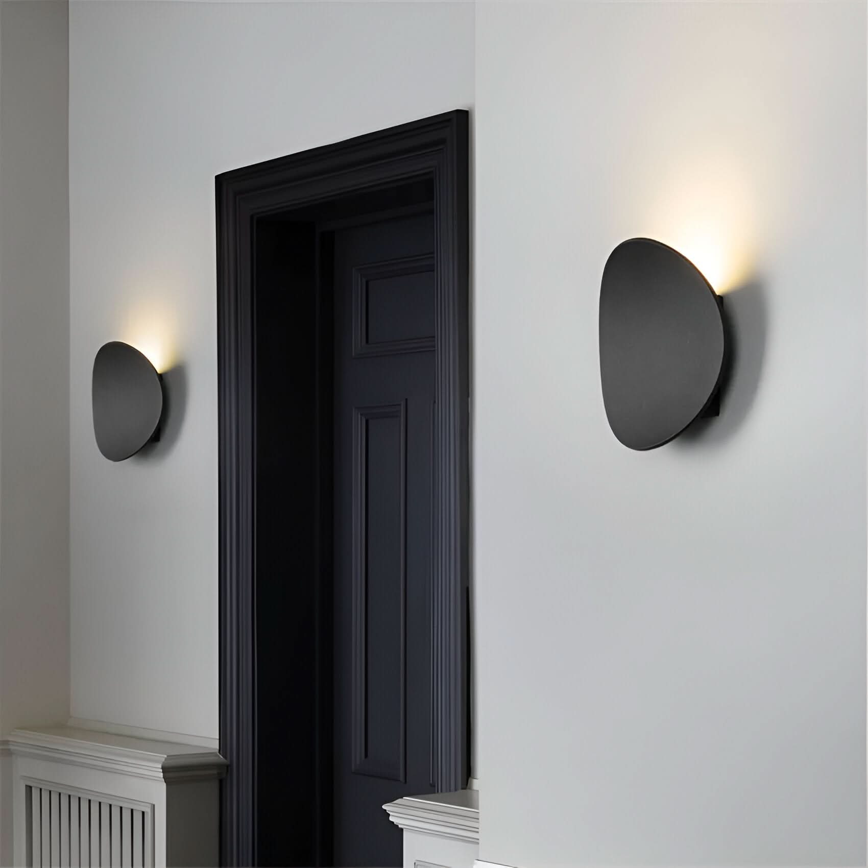 Two modern wall lights on a white wall with a dark door in the background.