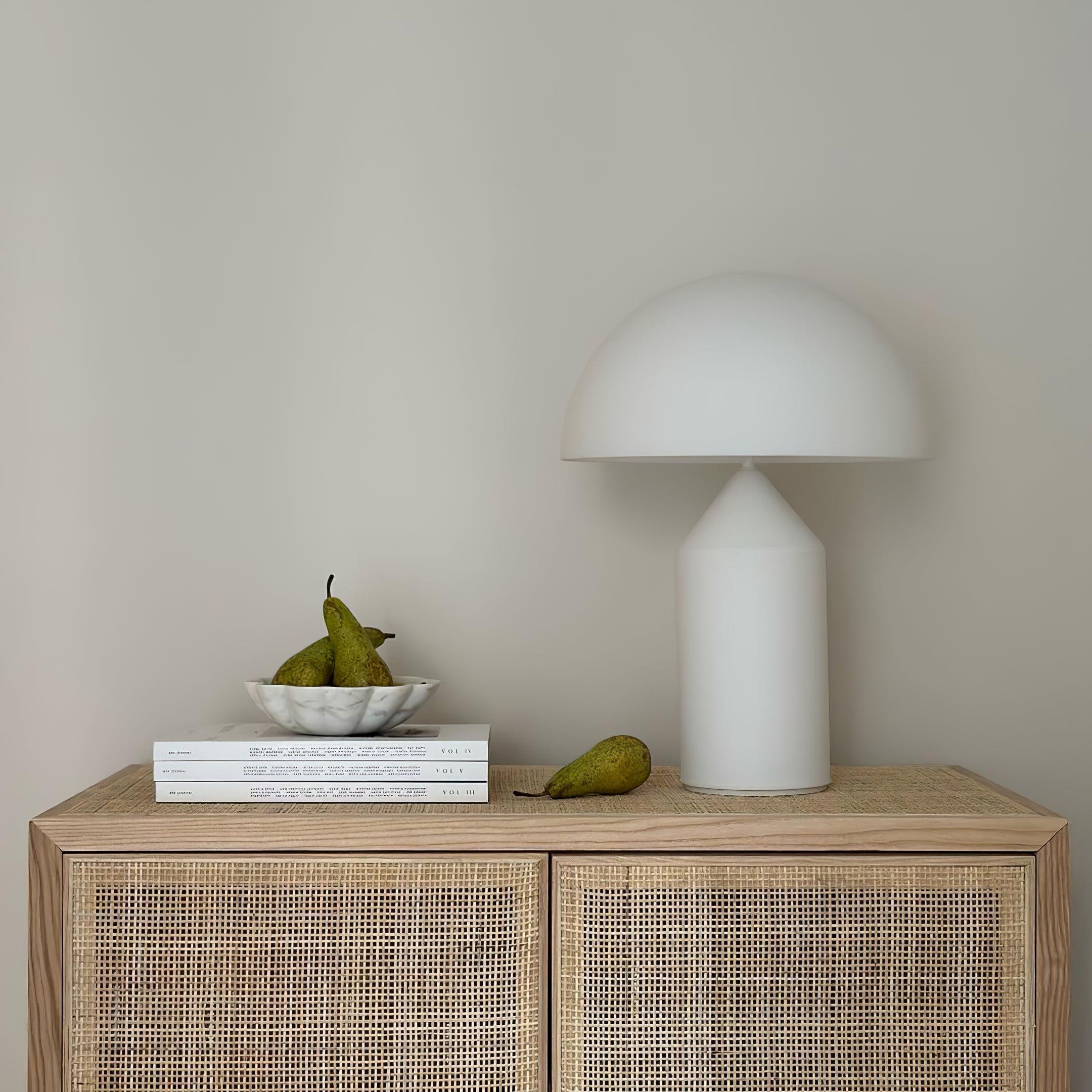 White lamp on a wooden cabinet with books and pears against a plain wall