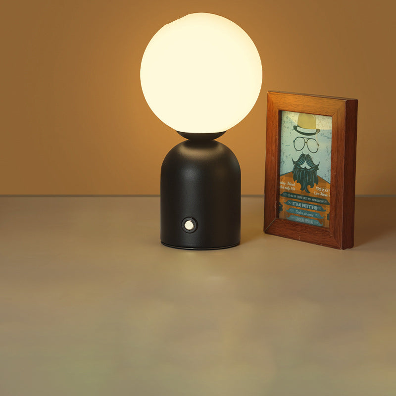 Black table lamp with a round white bulb next to a framed picture on a beige surface.