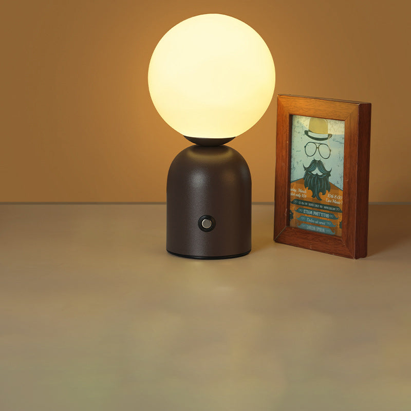 Table lamp with a round bulb on a dark brown base next to a framed picture on a beige surface.