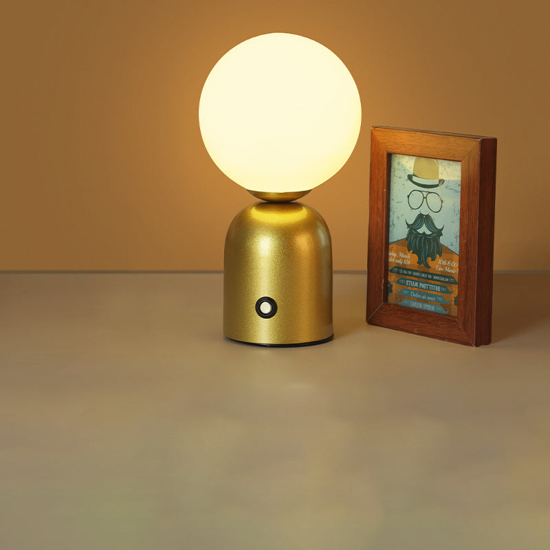 Gold table lamp with a round white bulb on a beige surface next to a framed picture.