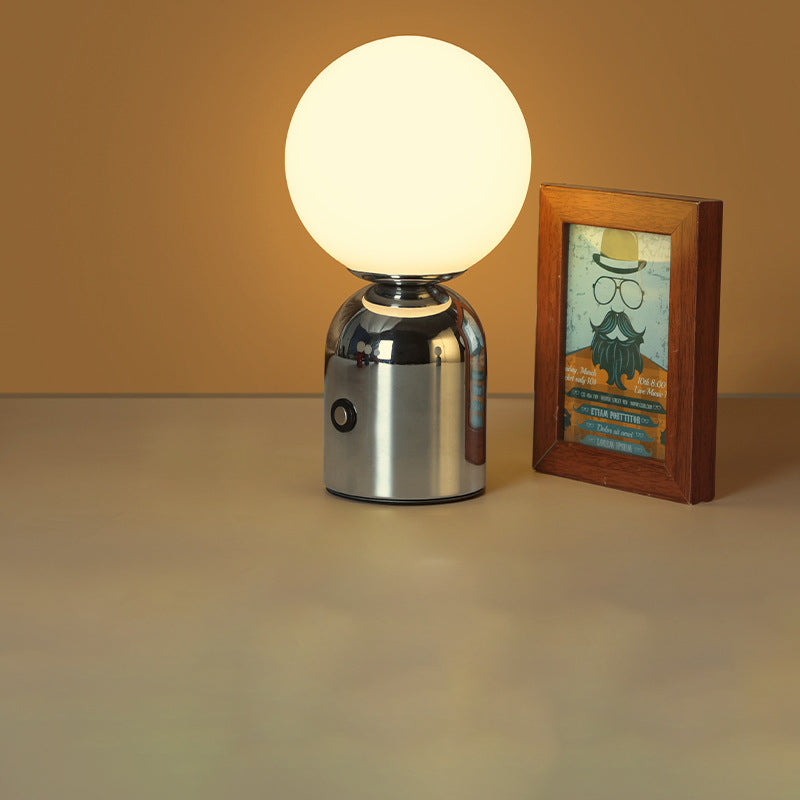 Table lamp with a round glass shade next to a framed picture on a beige surface.