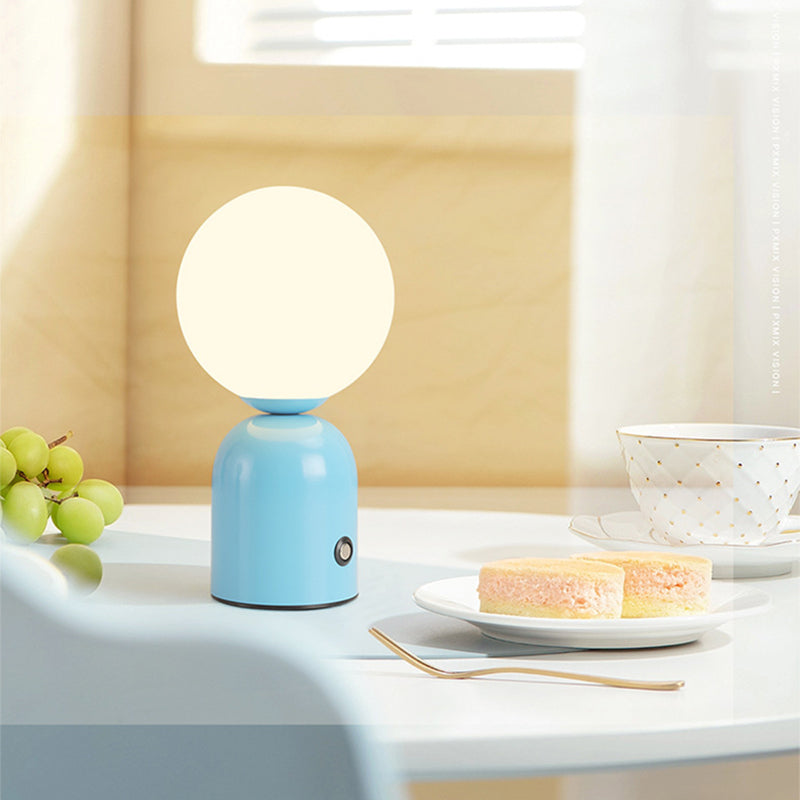 Blue table lamp with a white globe shade on a table with a cake and grapes.