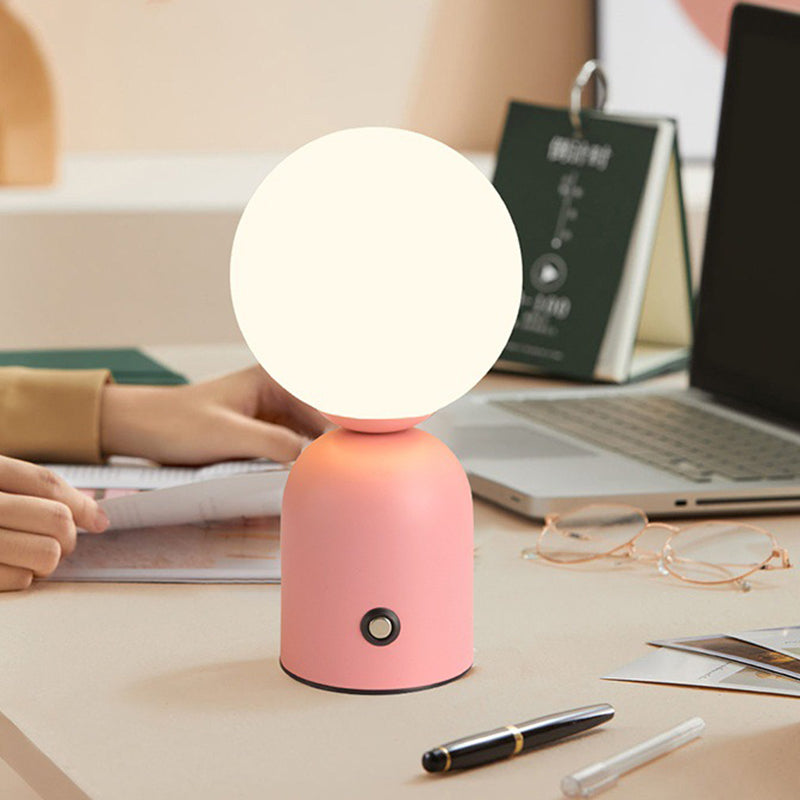Pink table lamp on a desk with a laptop and books in the background