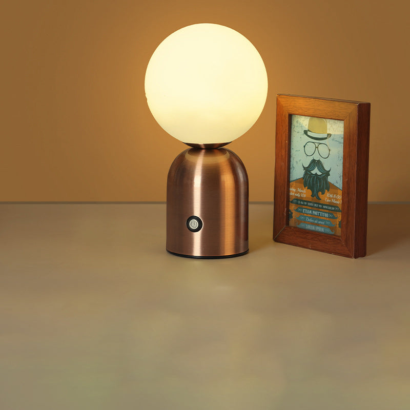 Copper table lamp with a round white bulb next to a framed picture on a beige surface.