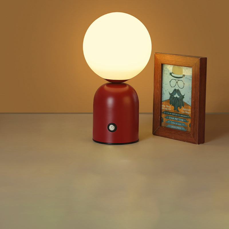 Red table lamp with a white globe shade next to a framed picture on a beige surface.