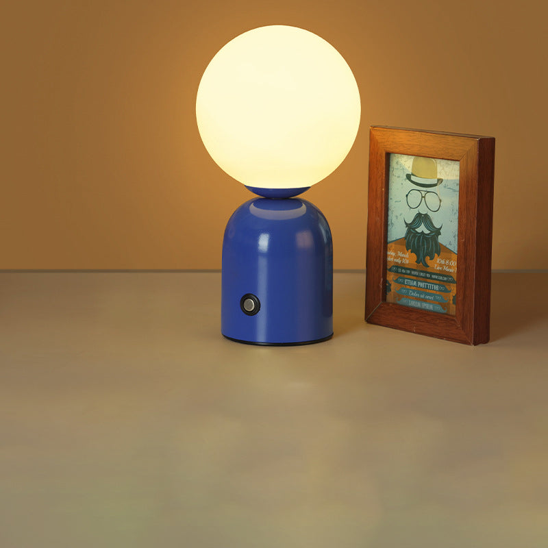 Blue table lamp with a round white bulb next to a framed picture on a beige surface.