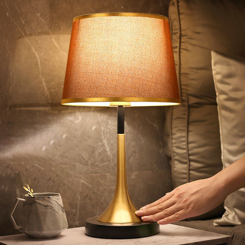 Table lamp with a textured brown shade and gold base on a marble surface.