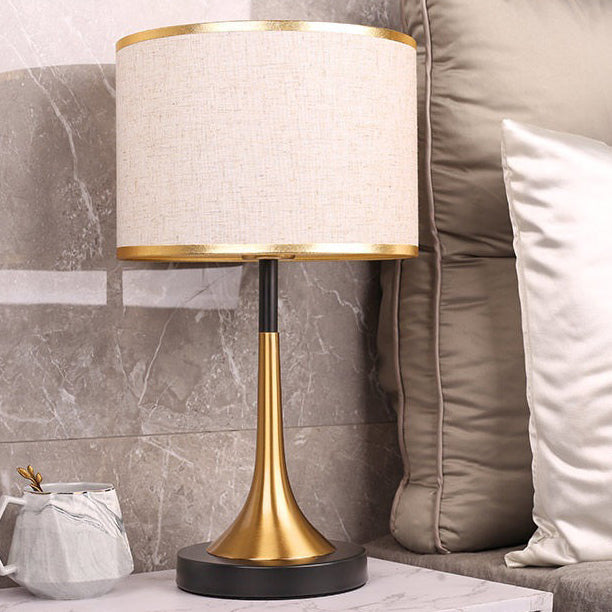 Table lamp with gold base and white shade on a marble surface next to a sofa.